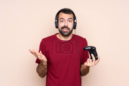Mann spielt mit Videospielsteuerung über isolierte Mauer und macht Geste des Zweifels