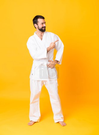 Photo for Full-length shot of man over isolated yellow background doing karate and pointing to the lateral - Royalty Free Image