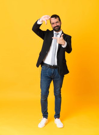 Foto de Una toma completa de hombre de negocios sobre un fondo amarillo aislado enfocando la cara. Símbolo de encuadre - Imagen libre de derechos