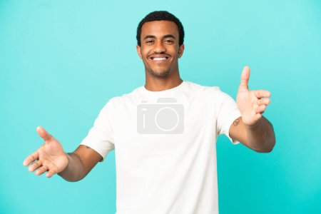 Téléchargez les photos : Afro-américain bel homme sur fond bleu isolé présentant et invitant à venir avec la main - en image libre de droit