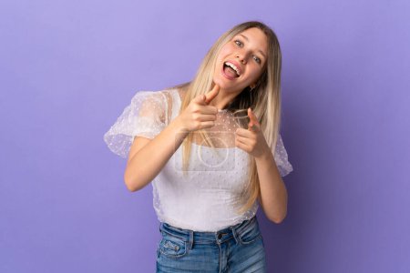 Photo for Young blonde woman isolated on purple background pointing to the front and smiling - Royalty Free Image