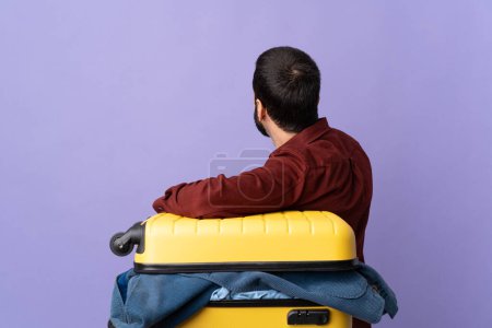 Photo for Traveler caucasian man with a suitcase full of clothes over isolated purple background in back position - Royalty Free Image