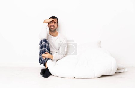 Foto de Caucásico hombre en pijama sentado en el suelo en interiores con dolor de cabeza - Imagen libre de derechos