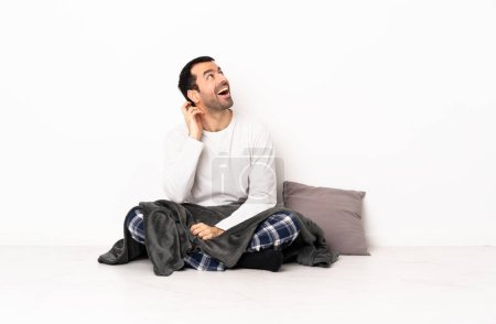 Téléchargez les photos : Homme caucasien en pyjama assis sur le sol à l'intérieur pensant une idée - en image libre de droit
