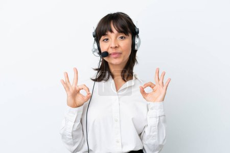 Foto de Telemarketer mujer de raza mixta trabajando con un auricular aislado sobre fondo blanco que muestra un signo de ok con los dedos - Imagen libre de derechos