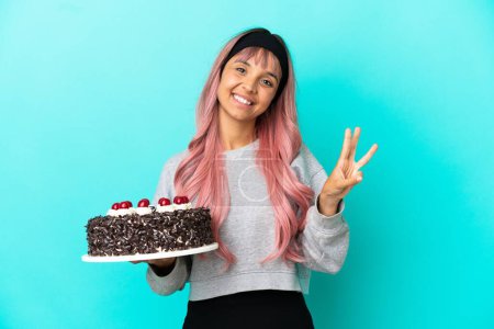 Photo for Young woman with pink hair holding birthday cake isolated on blue background happy and counting three with fingers - Royalty Free Image