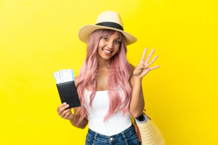 Foto de Joven mujer de raza mixta sosteniendo pasaporte y bolso de playa aislado sobre fondo amarillo feliz y contando cuatro con los dedos - Imagen libre de derechos