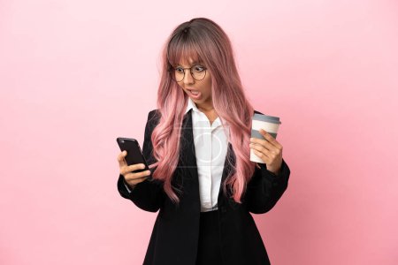 Téléchargez les photos : Jeune entreprise mixte femme aux cheveux roses isolé sur fond rose tenant café à emporter et un mobile - en image libre de droit
