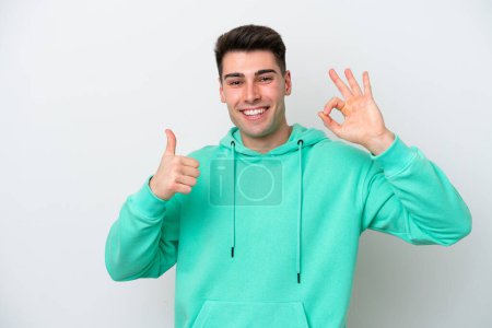 Foto de Joven hombre caucásico aislado sobre fondo blanco mostrando signo de ok y el pulgar hacia arriba gesto - Imagen libre de derechos
