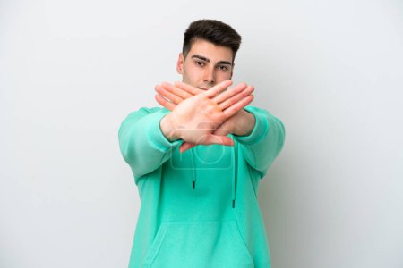 Foto de Joven hombre caucásico aislado sobre fondo blanco haciendo stop gesture con su mano para detener un acto - Imagen libre de derechos