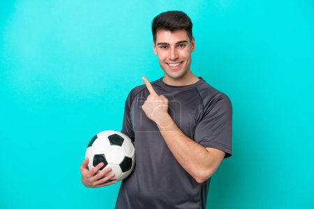 Foto de Joven futbolista caucásico aislado sobre fondo azul apuntando hacia un lado para presentar un producto - Imagen libre de derechos