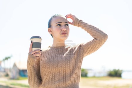 Photo for Young moroccan girl holding a take away coffee at outdoors having doubts and with confuse face expression - Royalty Free Image