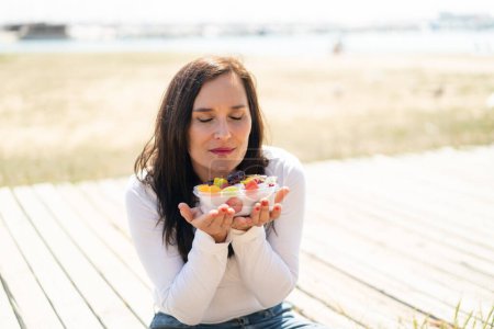 Téléchargez les photos : Femme d'âge moyen tenant un bol de fruits à l'extérieur - en image libre de droit