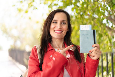 Foto de Mujer de mediana edad sosteniendo un pasaporte al aire libre y señalándolo - Imagen libre de derechos