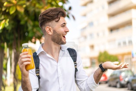 Téléchargez les photos : Young handsome man holding an orange juice at outdoors with surprise facial expression - en image libre de droit