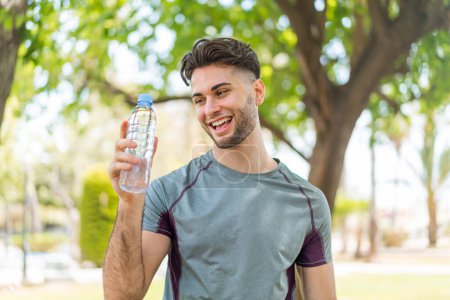 Photo for Young handsome sport man with a bottle of water at outdoors with happy expression - Royalty Free Image