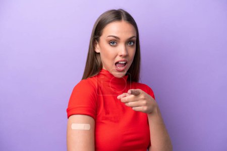 Téléchargez les photos : Jeune femme caucasienne portant un pansement isolé sur fond violet surpris et pointant devant - en image libre de droit