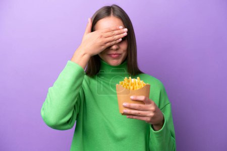 Photo for Young caucasian woman holding fried chips on purple background covering eyes by hands. Do not want to see something - Royalty Free Image