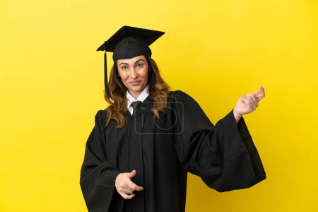 Foto de Graduado universitario de mediana edad aislado sobre fondo amarillo haciendo gesto de guitarra - Imagen libre de derechos