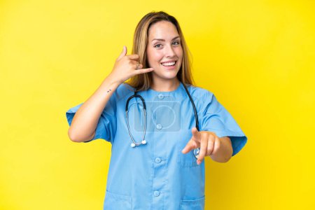 Téléchargez les photos : Jeune chirurgien infirmière femme isolée sur fond jaune faisant geste téléphonique et pointant vers l'avant - en image libre de droit