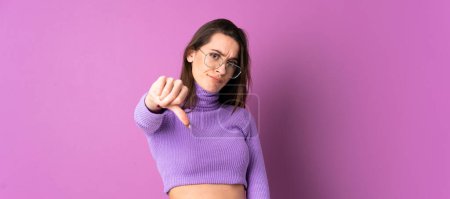 Téléchargez les photos : Jeune femme sur fond violet isolé montrant pouce vers le bas avec expression négative - en image libre de droit