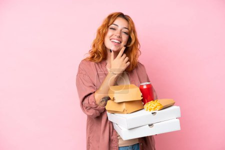 Photo for Young caucasian woman holding fast food isolated on pink background happy and smiling - Royalty Free Image