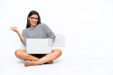 Téléchargez les photos : Young caucasian woman with a laptop sitting on the floor making guitar gesture - en image libre de droit