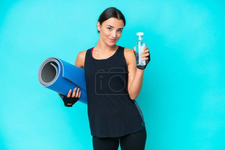 Foto de Mujer joven caucásica aislada sobre fondo azul con botella de agua deportiva y con una esterilla - Imagen libre de derechos