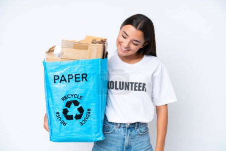 Foto de Joven mujer caucásica sosteniendo una bolsa de reciclaje llena de papel para reciclar aislada sobre fondo blanco con expresión feliz - Imagen libre de derechos