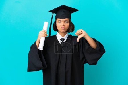 Foto de Joven universitaria graduada sobre fondo azul aislado mostrando el pulgar hacia abajo con dos manos - Imagen libre de derechos