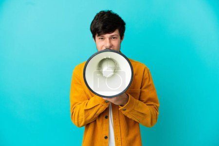 Photo for Young Russian man isolated on blue background shouting through a megaphone to announce something - Royalty Free Image