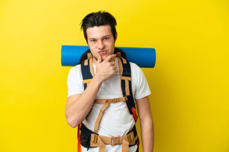 Photo for Young mountaineer Russian man with a big backpack isolated on yellow background thinking - Royalty Free Image