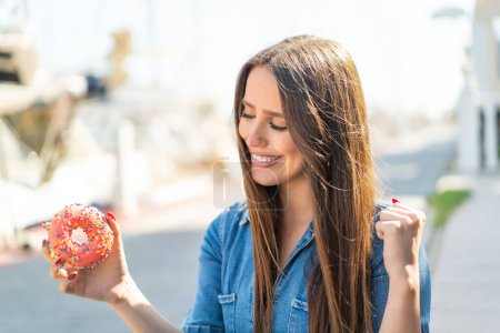 Foto de Mujer joven sosteniendo un donut al aire libre celebrando una victoria - Imagen libre de derechos
