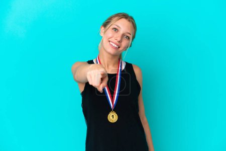 Téléchargez les photos : Jeune femme caucasienne avec des médailles isolées sur fond bleu pointe doigt à vous avec une expression confiante - en image libre de droit