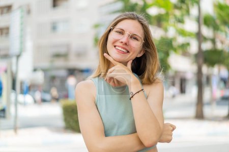 Téléchargez les photos : Jeune femme blonde avec des lunettes à l'extérieur souriant - en image libre de droit