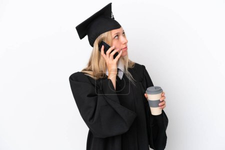 Téléchargez les photos : Jeune diplômée universitaire caucasienne isolée sur fond blanc tenant café à emporter et un mobile - en image libre de droit