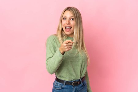 Téléchargez les photos : Jeune femme blonde isolée sur fond rose surprise et pointant devant - en image libre de droit
