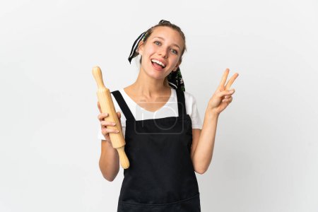 Photo for Young woman holding a rolling pin isolated on white background smiling and showing victory sign - Royalty Free Image