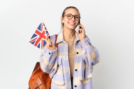 Téléchargez les photos : Jeune femme blonde tenant un drapeau du Royaume-Uni isolé sur fond blanc gardant une conversation avec le téléphone portable - en image libre de droit