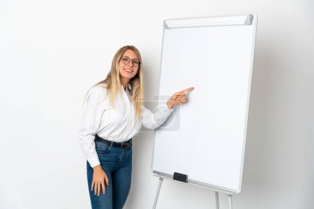 Mujer rubia joven aislada sobre fondo blanco dando una presentación sobre pizarra blanca y escribiendo en ella