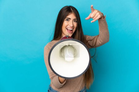 Photo for Young caucasian woman isolated on blue background shouting through a megaphone to announce something while pointing to the front - Royalty Free Image