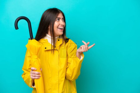 Young caucasian woman with rainproof coat and umbrella isolated on blue background intending to realizes the solution while lifting a finger up