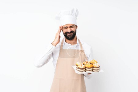 Photo for Young man holding muffin cake over isolated white background with headache - Royalty Free Image