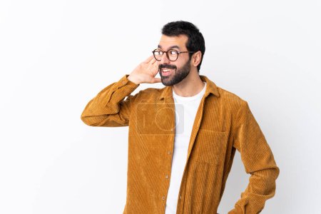 Foto de Caucásico hombre guapo con barba usando una chaqueta de pana sobre fondo blanco aislado escuchando algo poniendo la mano en la oreja - Imagen libre de derechos