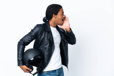 Téléchargez les photos : African American man with braids holding a motorcycle helmet isolated on white background shouting with mouth wide open to the side - en image libre de droit