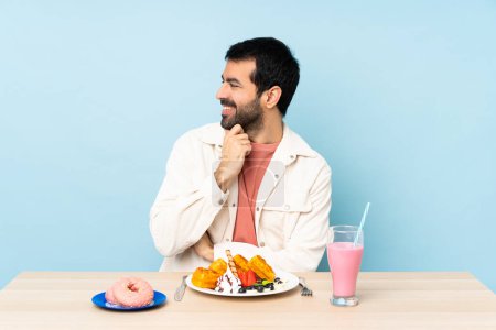 Foto de Hombre en una mesa desayunando gofres y un batido mirando hacia un lado - Imagen libre de derechos