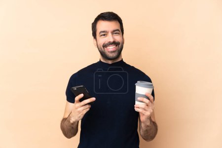 Téléchargez les photos : Blanc bel homme sur fond isolé tenant café à emporter et un mobile - en image libre de droit