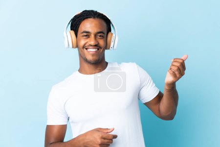 Photo for Young African American man with braids isolated on blue background listening music and doing guitar gesture - Royalty Free Image