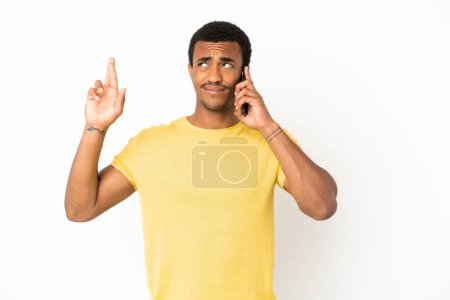 Téléchargez les photos : Afro-Américain bel homme utilisant un téléphone mobile sur fond blanc isolé avec les doigts croisés et souhaitant le meilleur - en image libre de droit