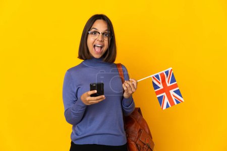 Téléchargez les photos : Jeune femme latine tenant un drapeau du Royaume-Uni isolé sur fond jaune surprise et envoyant un message - en image libre de droit